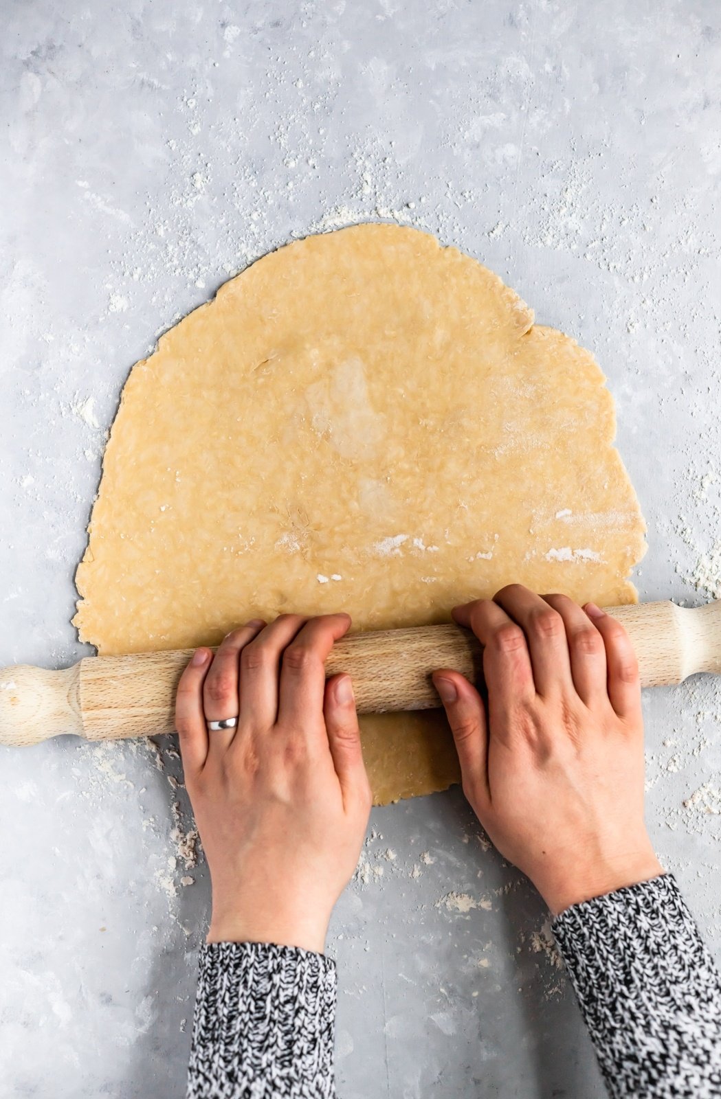 two hands using a rolling pin to roll out all butter pie dough