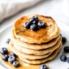 stack of pancakes on a plate topped with blueberries and maple syrup