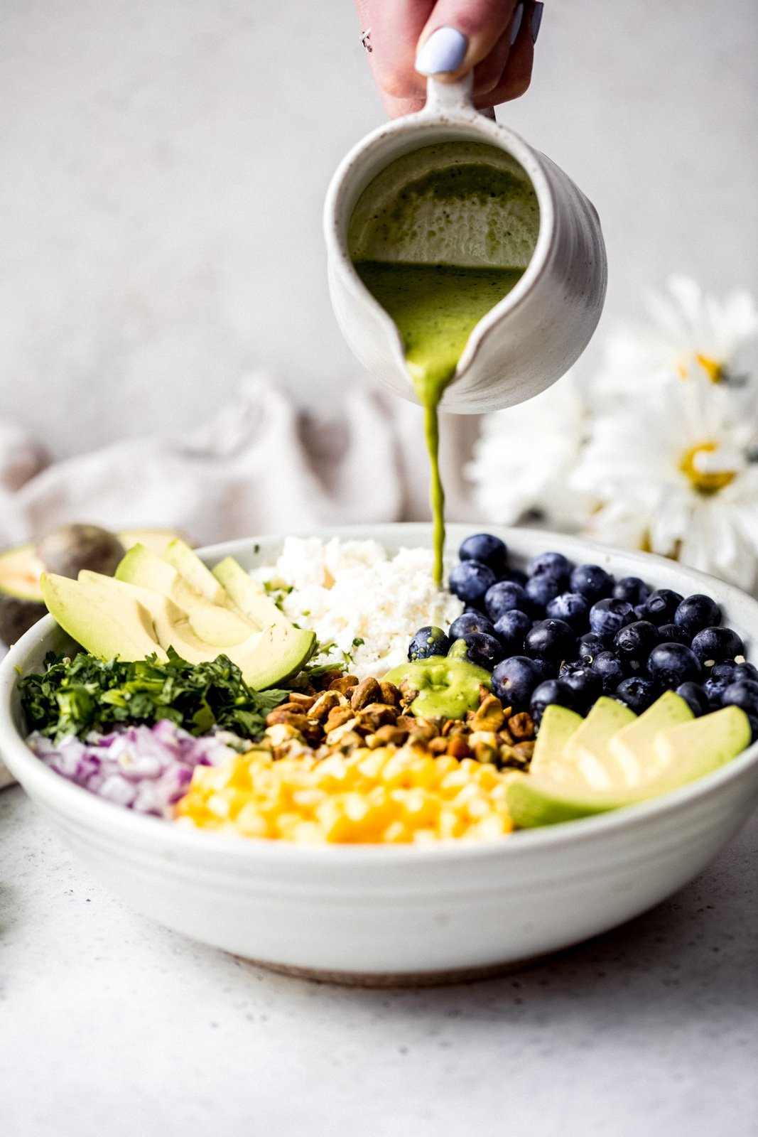 pouring dressing onto an avocado blueberry quinoa salad