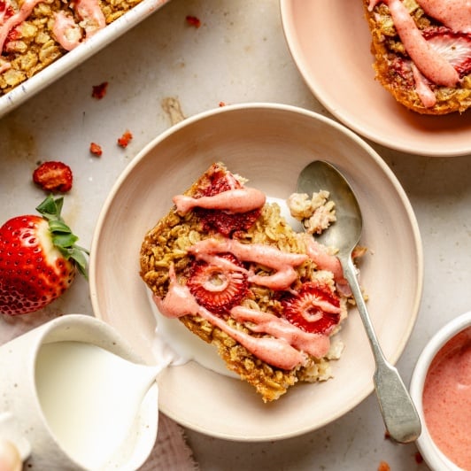 pouring milk into a bowl with a slice of strawberry baked oatmeal