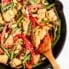 orange chicken stir fry in a skillet pan with a wooden spoon