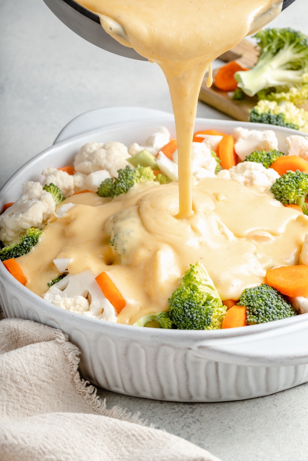 pouring cheddar cheese sauce over veggies for a broccoli cauliflower gratin