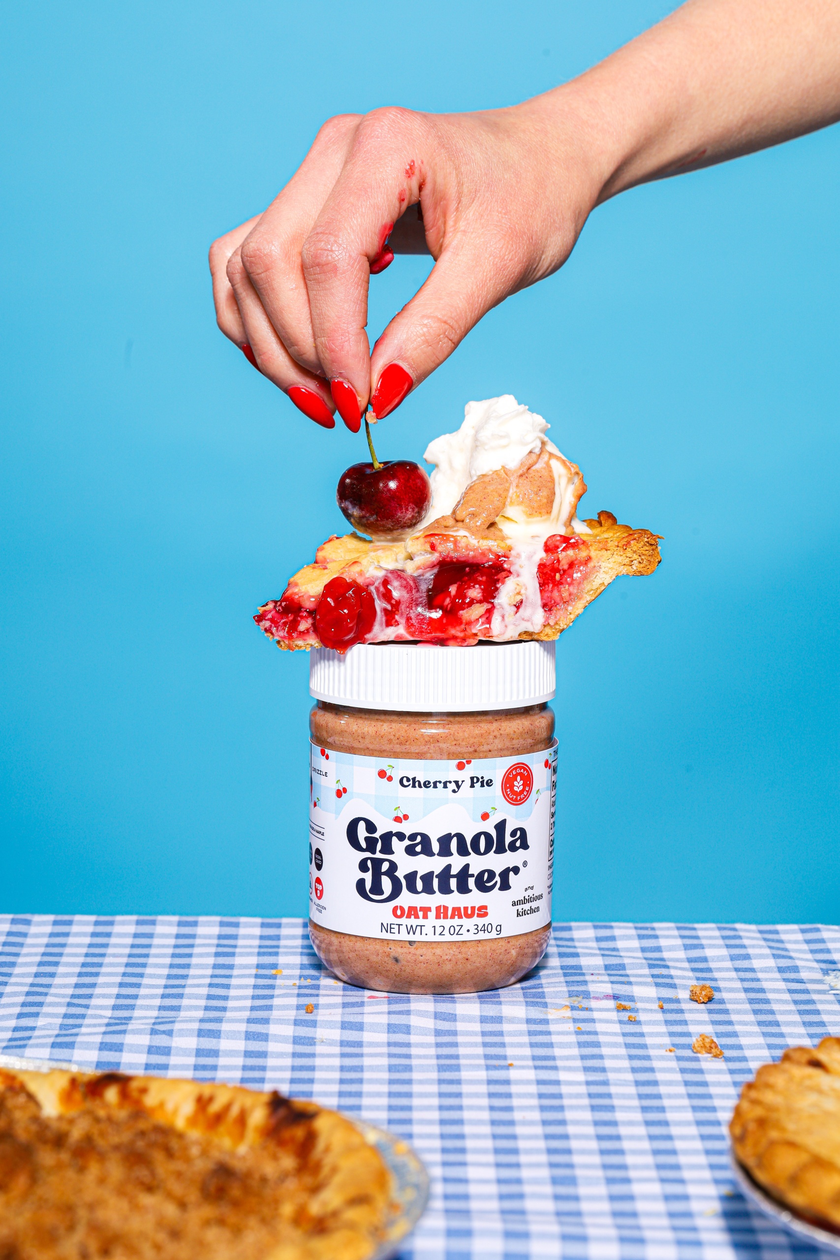 hand placing a cherry on top of a piece of cherry pie on top of a jar of Cherry Pie Granola Butter