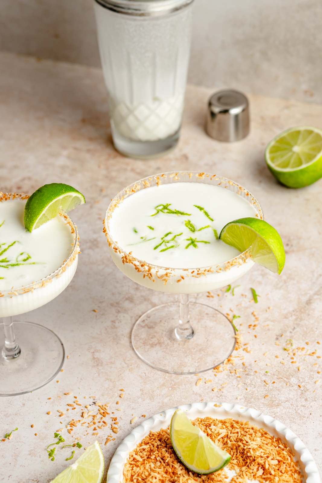 coconut margaritas in glasses next to toasted coconut and limes