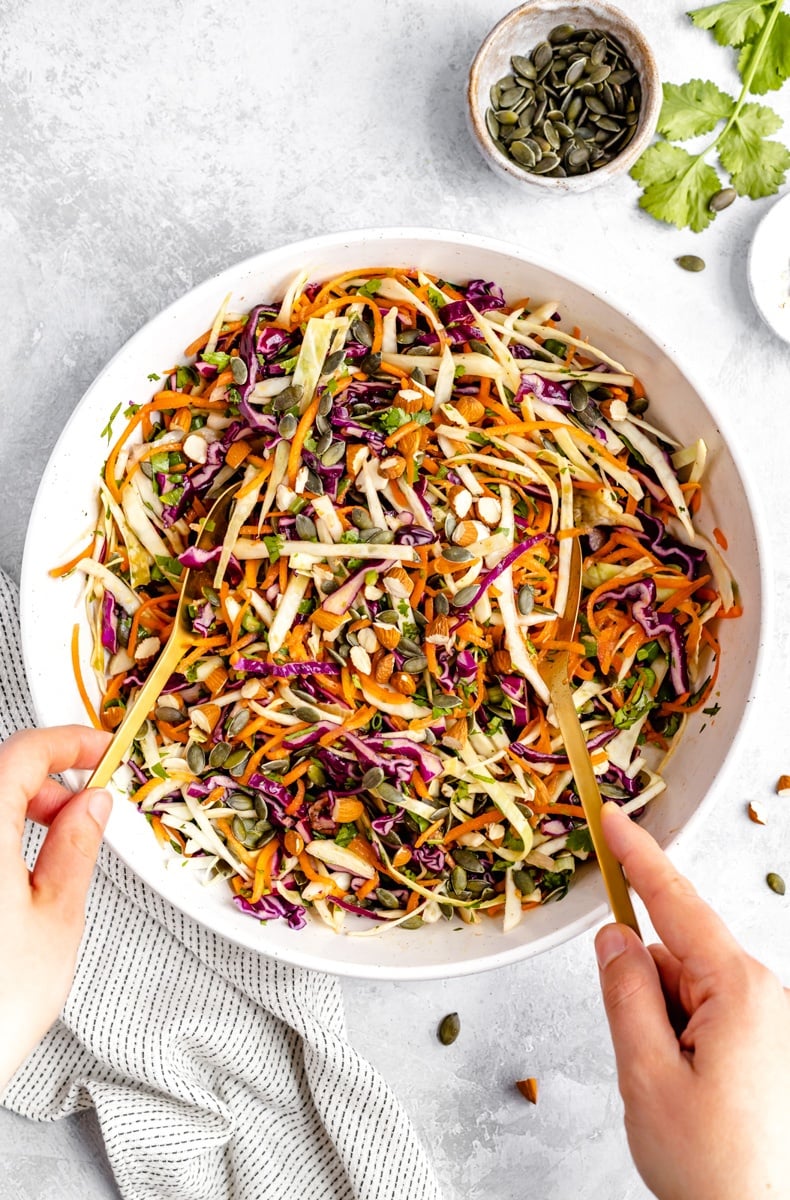 healthy coleslaw being mixing a bowl with two serving spoons