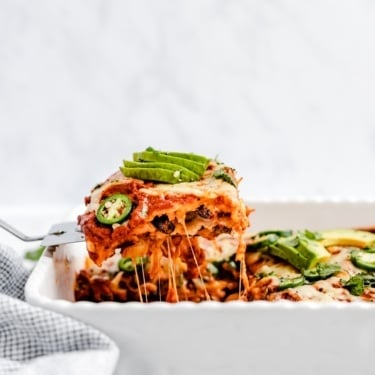 lifting a slice of healthy enchilada casserole out of a baking dish