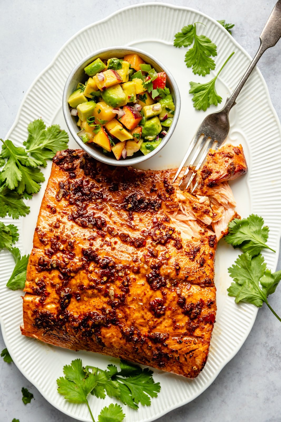 firecracker salmon on a platter next to a bowl of peach salsa