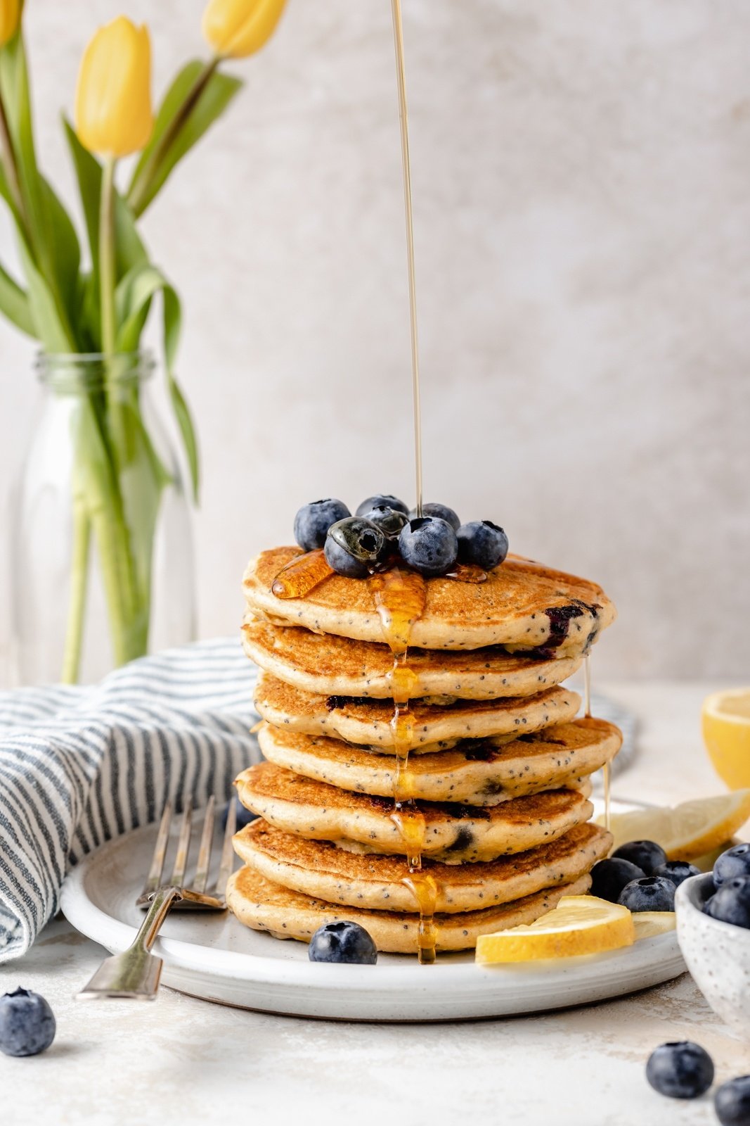 drizzling syrup onto a stack of gluten free lemon blueberry pancakes