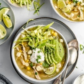 chicken pozole in two bowls topped with avocado, yogurt and cabbage