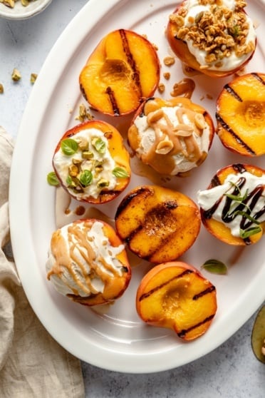 grilled peaches on a platter with different toppings