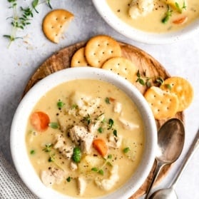 healthy chicken pot pie soup in two bowls with crackers on the site