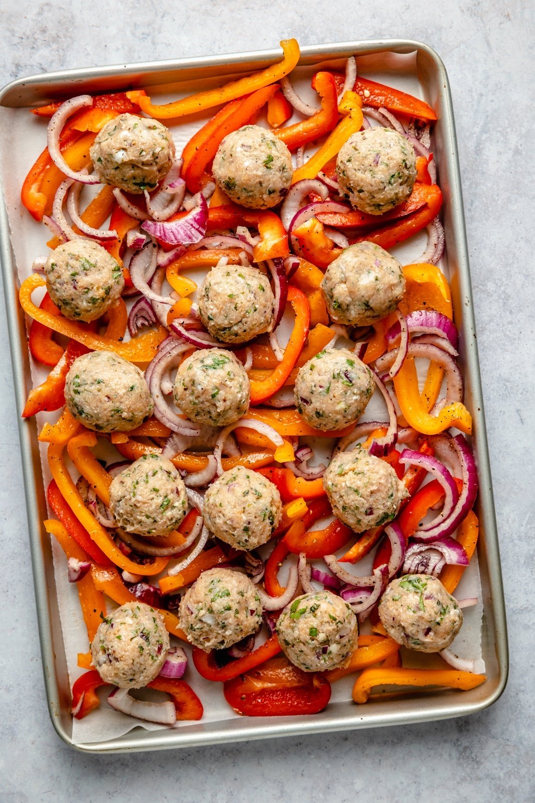 unbaked Greek turkey meatballs and peppers on a sheet pan