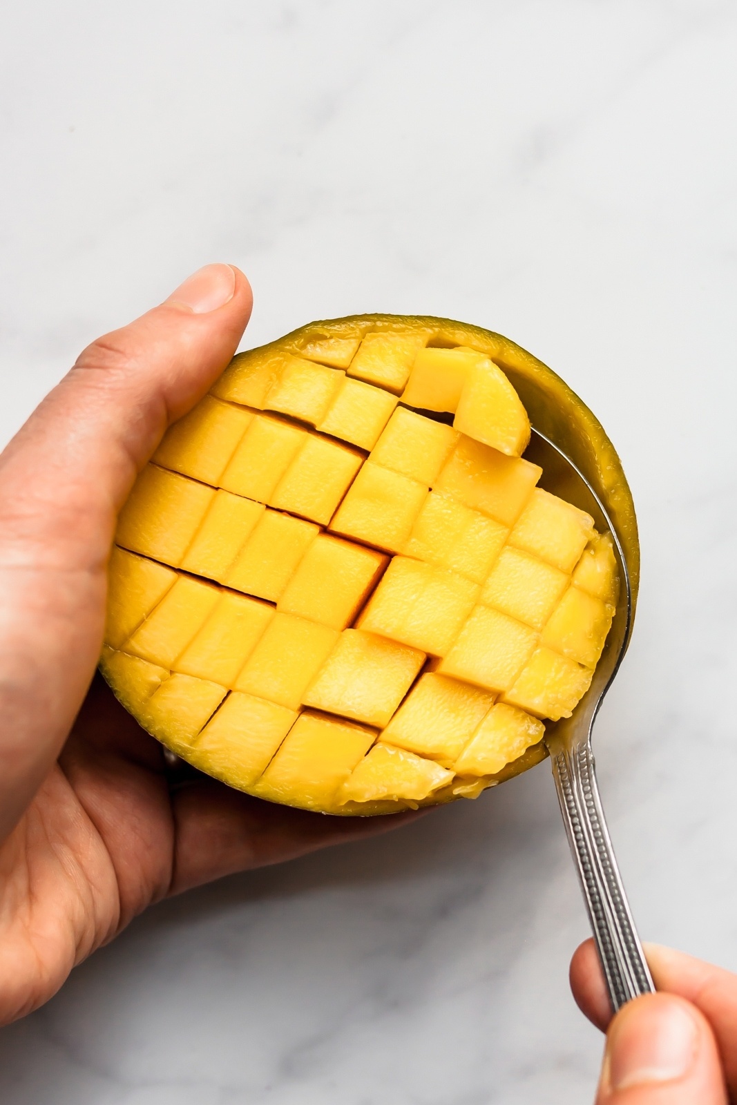 scooping mango cubes out of half of a mango