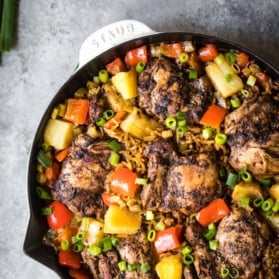 caribbean jerk chicken in a skillet with rice, pineapple, and red peppers