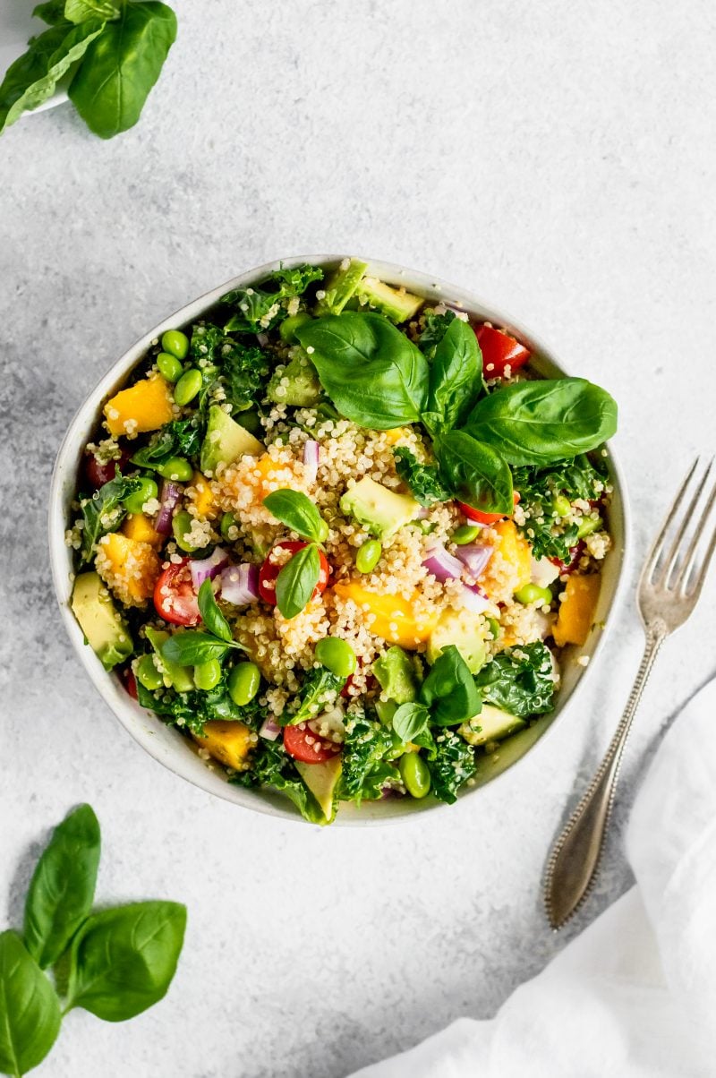 Kale quinoa salad with mango and edamame in a bowl next to a fork