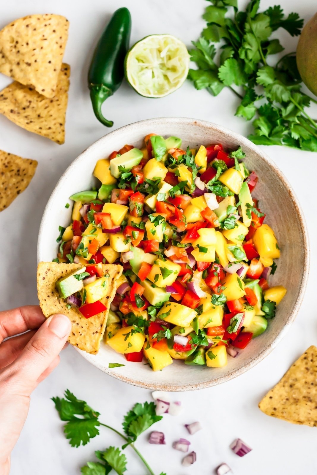 overhead shot of a chip dipping into a bowl of mango salsa