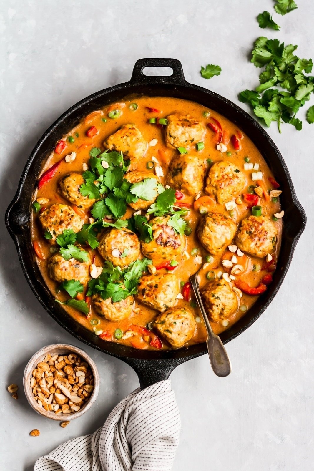 ginger chicken meatballs in a skillet with peanut sauce and a spoon