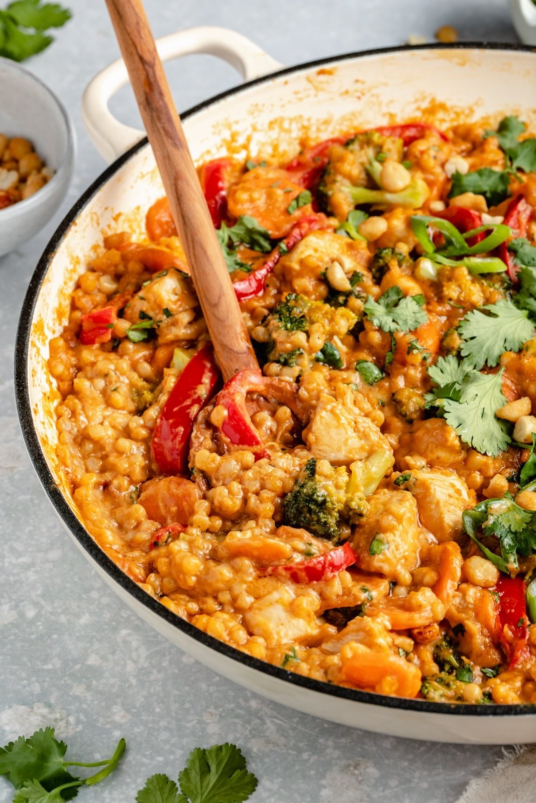 Thai peanut chicken couscous in a skillet with a wooden spoon