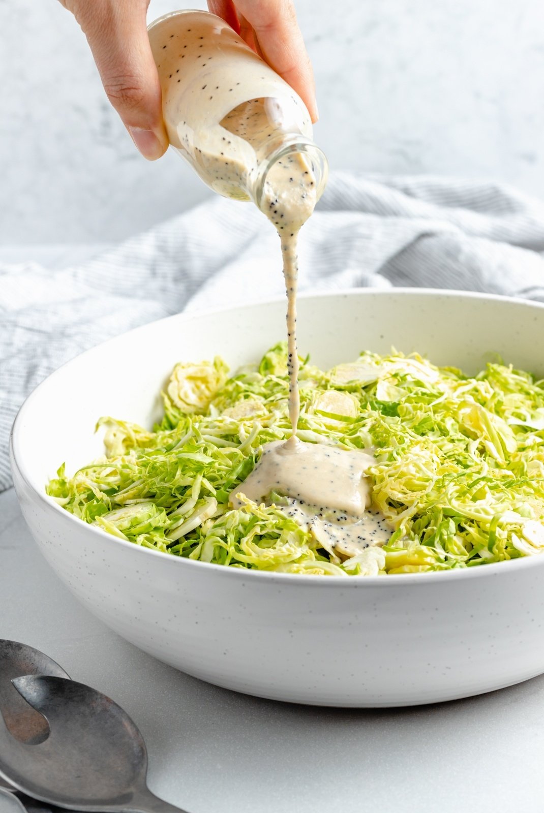 pouring tahini poppy seed dressing into a bowl of brussels sprouts