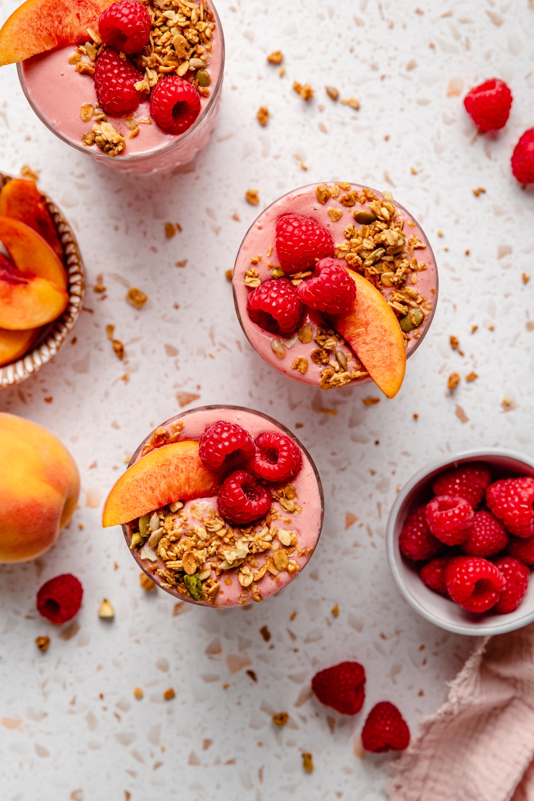 top-down view of peach smoothies in glasses topped with granola and raspberries