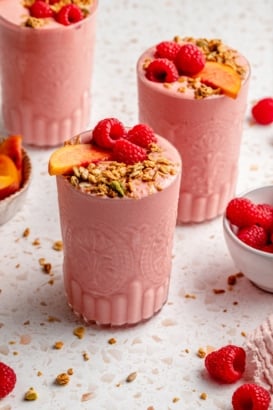 peach smoothie in glasses topped with granola and fruit