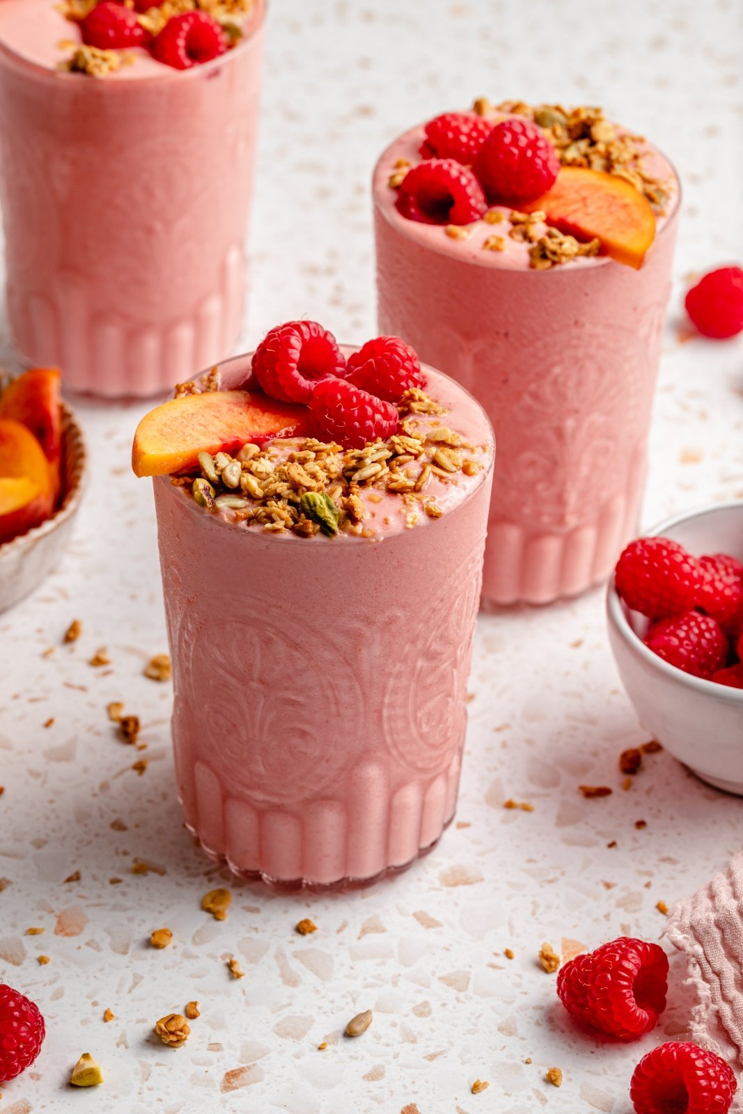 healthy peach smoothie in three glasses topped with fruit and granola