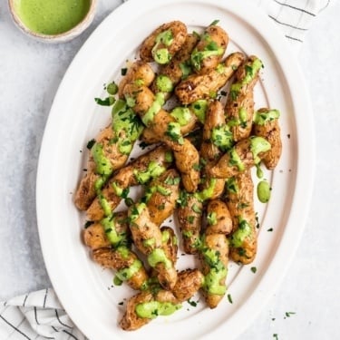 roasted garlic fingerling potatoes drizzled with green sauce on a platter