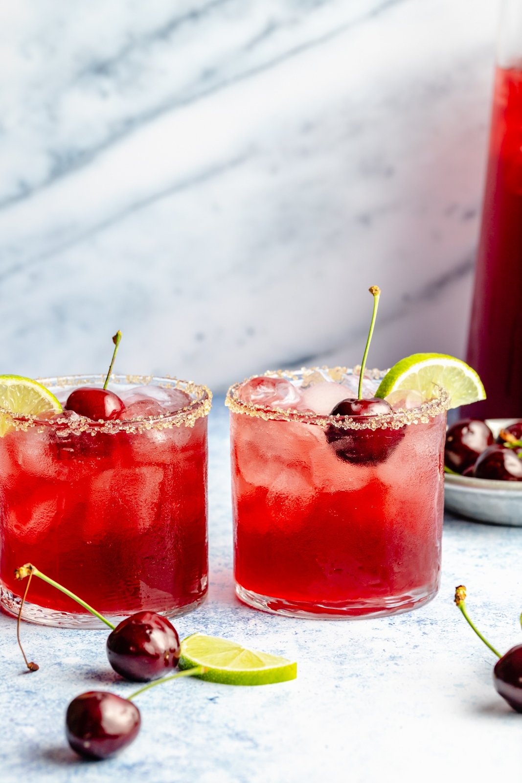 two cherry lime cocktails next to fresh cherries