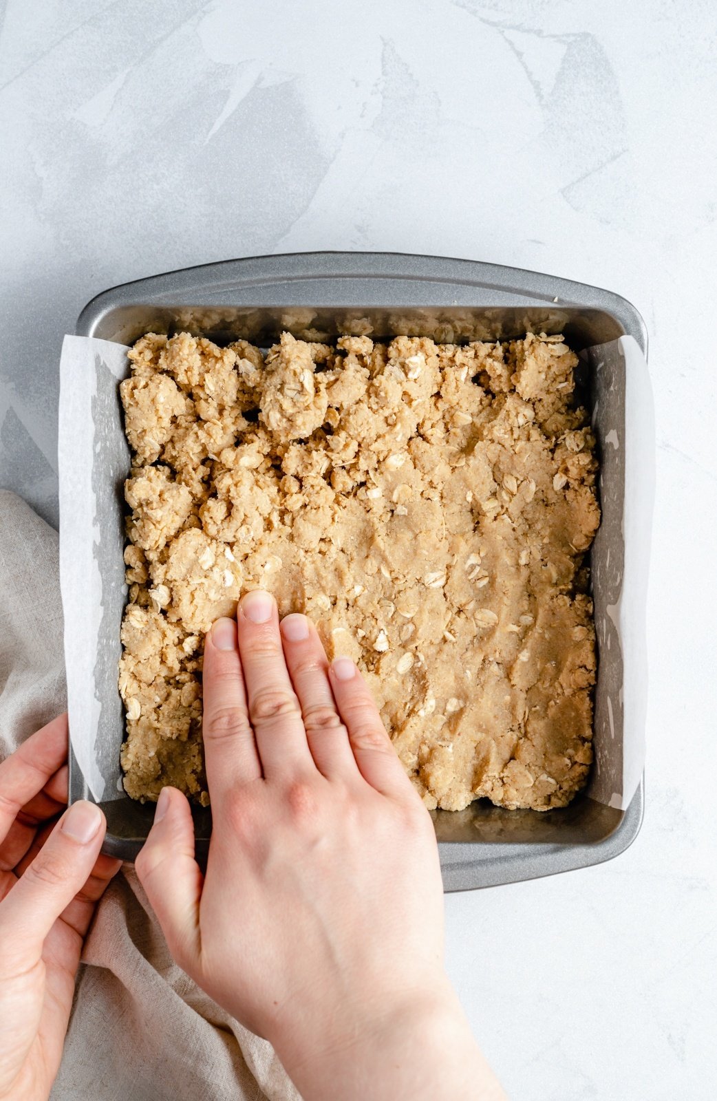 pressing a crust into a pan for strawberry oatmeal bars