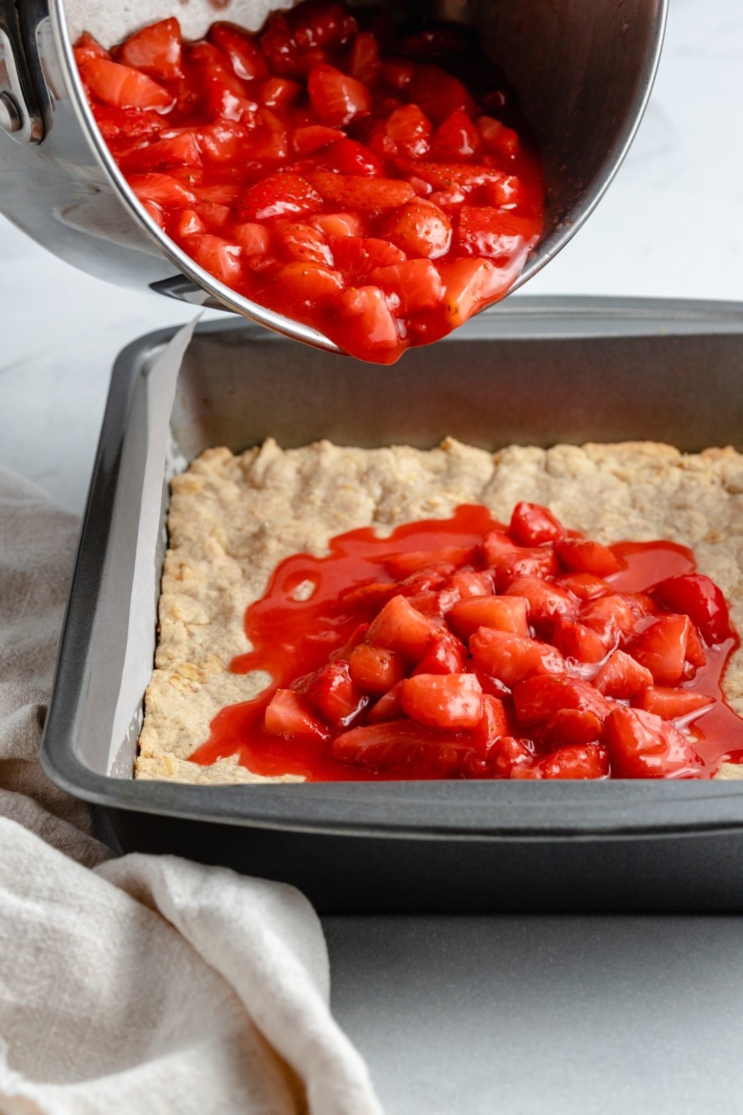 pouring strawberry filling onto a crust for healthy strawberry crumble bars