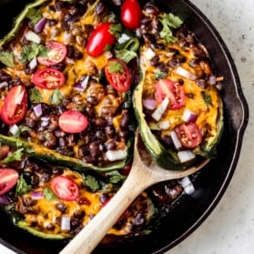 grilled stuffed poblano peppers in a skillet with a wooden spoon