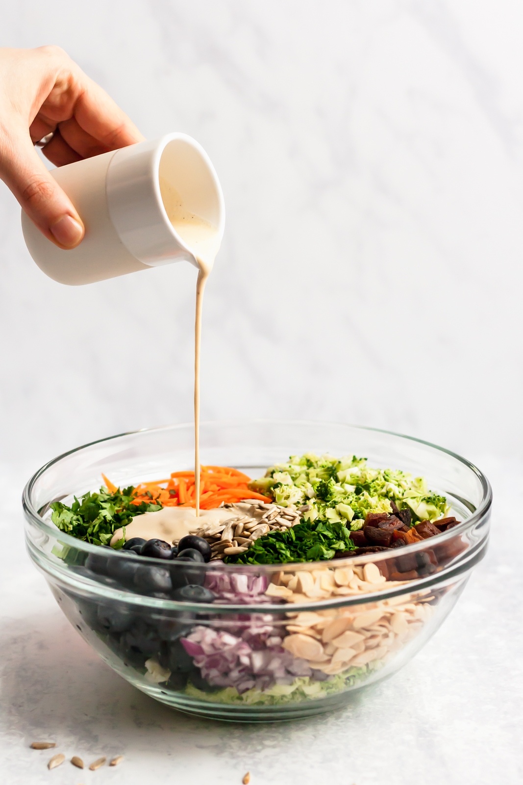 pouring dairy free dressing into a bowl with a healthy broccoli salad