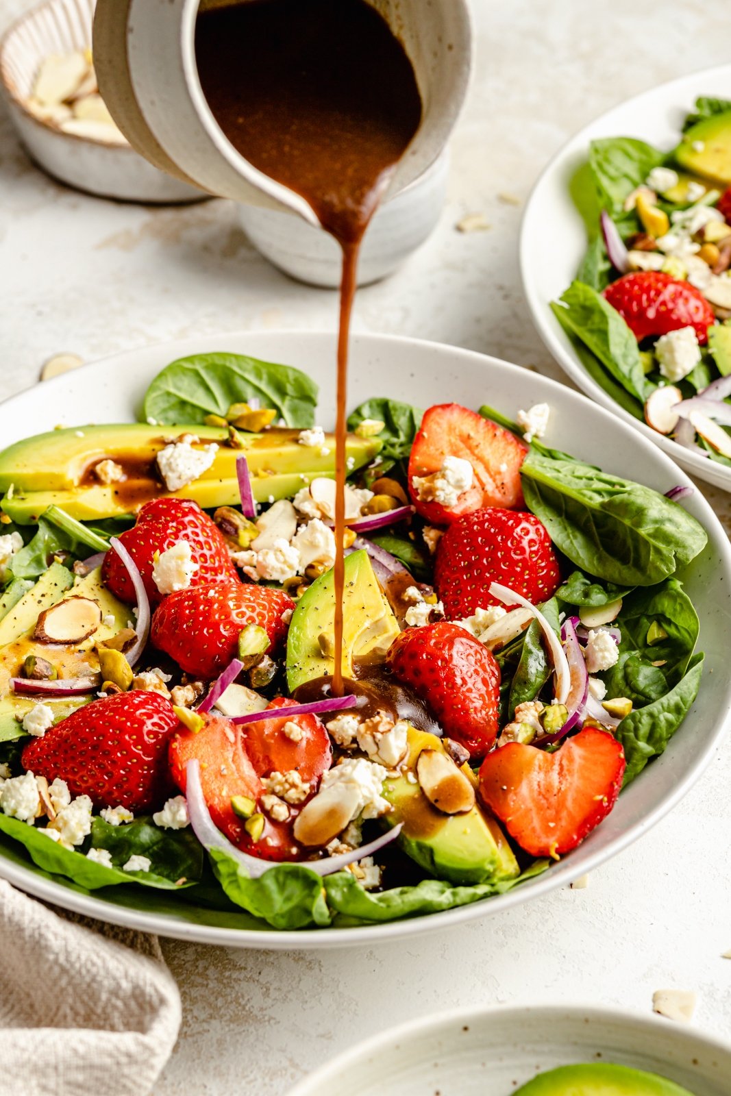 pouring dressing onto a strawberry spinach salad