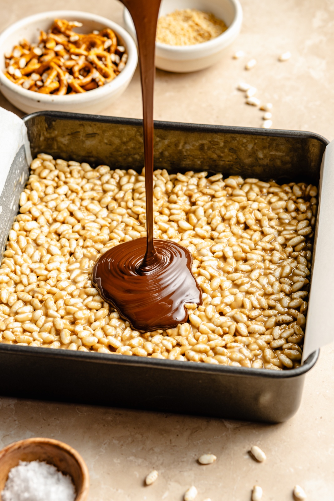 pouring chocolate on top of tahini rice krispie treats in a pan