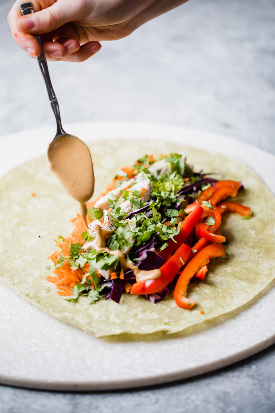 drizzling peanut sauce onto a thai peanut chicken wrap