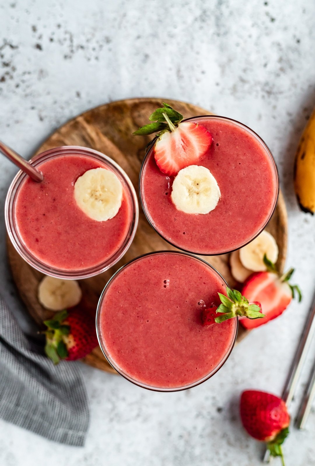 three strawberry orange banana smoothies on a wooden tray